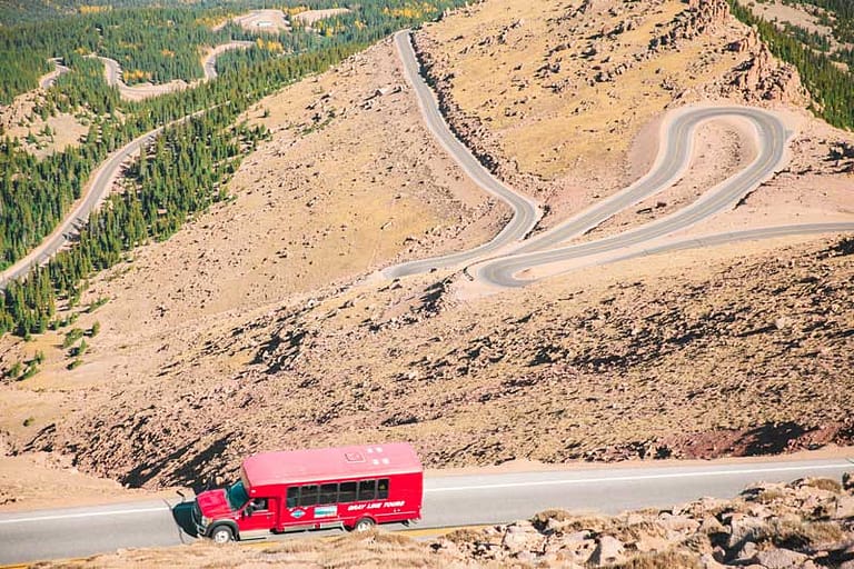 pikes peak tour by gray line red bus going up highway