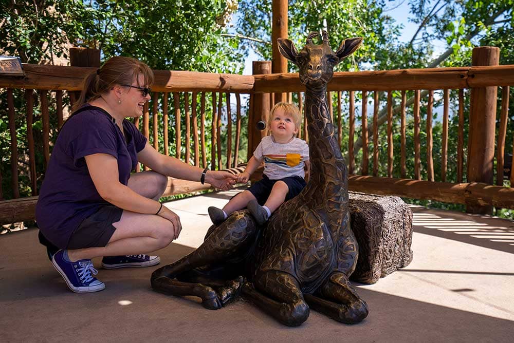 Baby sitting on giraffe statue at the Cheyenne Mountain Zoo