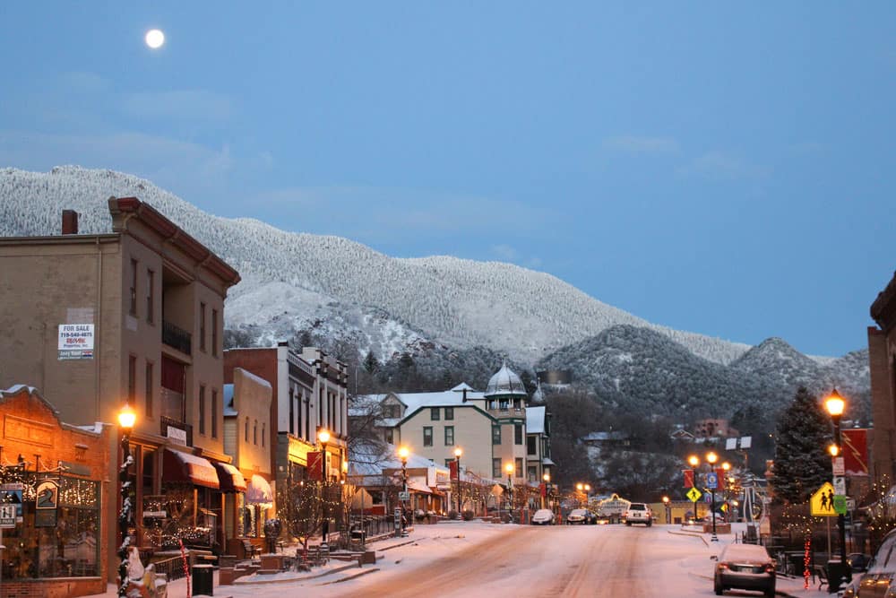 Historic downtown Manitou Springs on a snowy evening, with the full moon in the background.