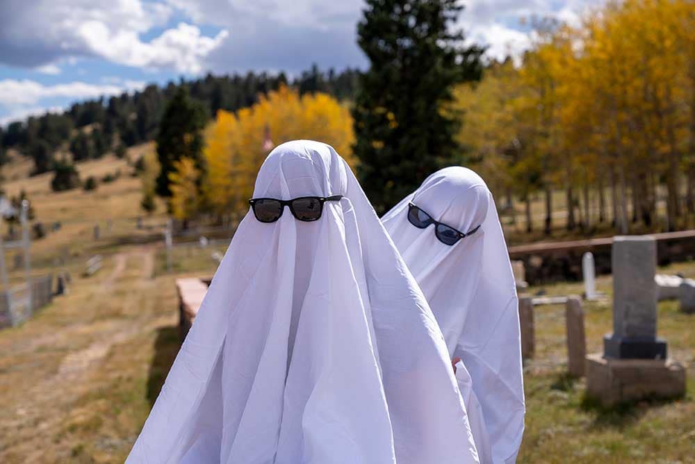 Dos humanos vestidos con trajes de fantasma y gafas de sol comparten historias de fantasmas de Pikes Peak en un cementerio de Cripple Creek.