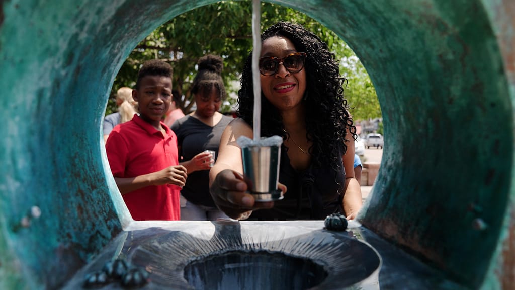 Woman filling a cup of water at mineral spring.