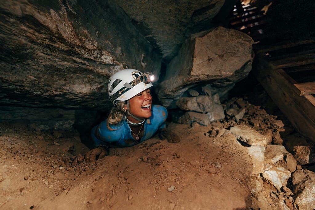 Woman climbing through hole in Cave of the Winds Expedition Tour