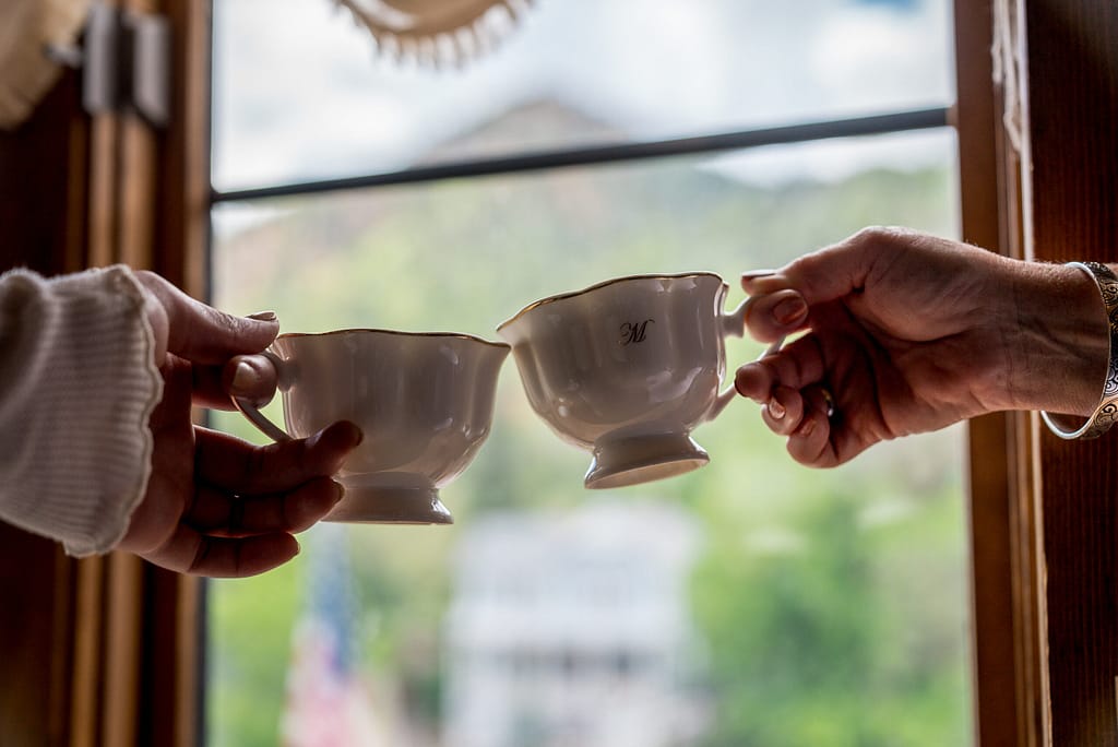 Hands clinking tea cups in front of window at Miramont Castle