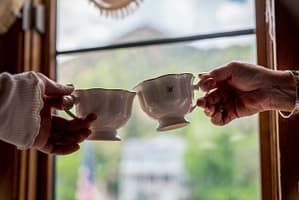 Hands clinking tea cups in front of window at Miramont Castle