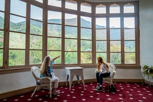 Women sitting in large room pointing out window at Miramont Castle