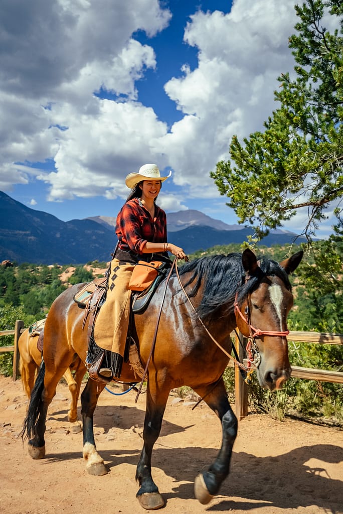 Cowgirl riding horse with Academy Riding Stables with Pikes Peak in the background
