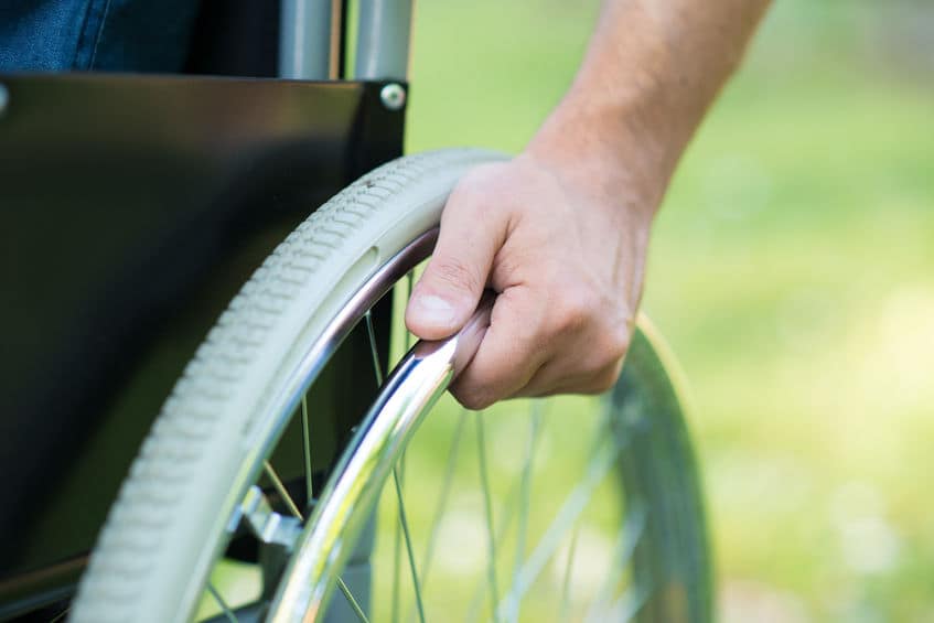 Close-up of a hand on a wheelchair wheel outdoors.